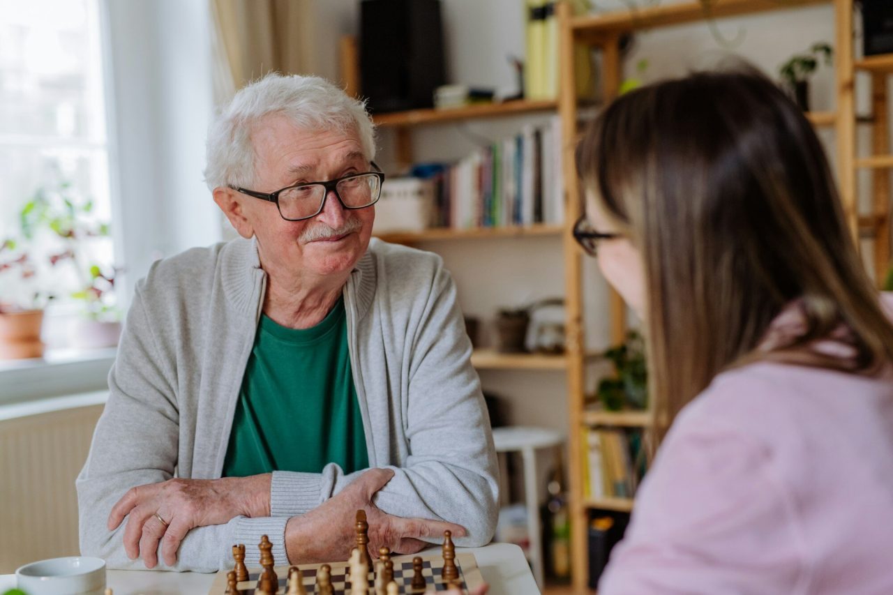 adult-daughter-visiting-her-senior-father-at-home-and-playing-chess-together-